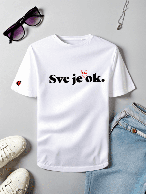 Bijela pamučna majica s natpisom "Sve je baš ok.", gdje je riječ "baš" naglašena crvenom bojom, a iznad slova "o" nalazi se mala ilustracija bubamare. Majica je postavljena na ravnu površinu uz modne dodatke – crne sunčane naočale s ljubičastim staklima, srebrnu ogrlicu, svijetloplave traperice i bijele tenisice.