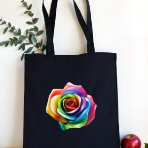 Crna platnena torba s dugim ručkama, ukrašena šarenom ružom u duginim bojama, postavljena na bijelu podlogu s grančicom zelenog lišća i svježim voćem u pozadini.