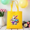 žuta platnena vrećica s uskršnjim motivom – preslatki smeđi zeko drži košaricu punu šarenih pisanica. Vrećica je postavljena na drveni stol, okružena pastelno obojenim balonima i cvijećem u pozadini.