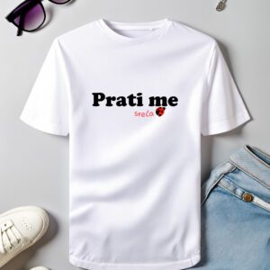 Bijela pamučna majica s natpisom 'Prati me sreća' i crvenim motivom bubamare, položena uz sunčane naočale, tenisice i traperice